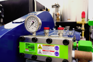 Jetstream hot water pressure washer pump with 15,000 psi gauge and safety warning labels for industrial cleaning